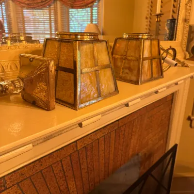 Pair of vintage Arts and Crafts style brass and slag glass wall sconces with tapered square shades, resting on a fireplace mantel.