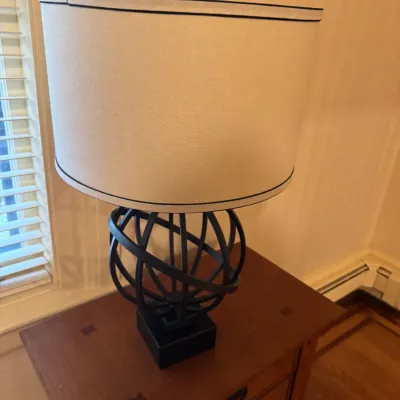 Modern black metal orb table lamp with an off-white drum shade, displayed atop a wood nightstand.