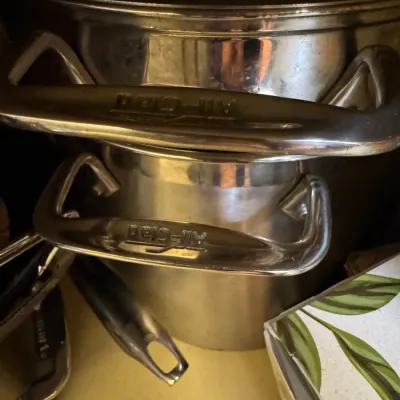 Stacked All-Clad stainless steel stockpots with double side handles, showing minor surface wear from use.