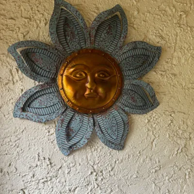 Southwestern-style metal sun face wall art featuring a repoussé copper-tone center surrounded by patterned verdigris-finish petals.