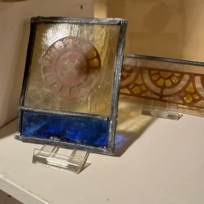 Pair of vintage leaded stained glass suncatchers displayed on acrylic stands, featuring geometric and medallion motifs in amber and...