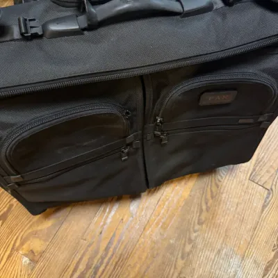 Black Tumi ballistic nylon wheeled garment bag featuring multiple exterior zippered compartments, durable carrying handles, and a...