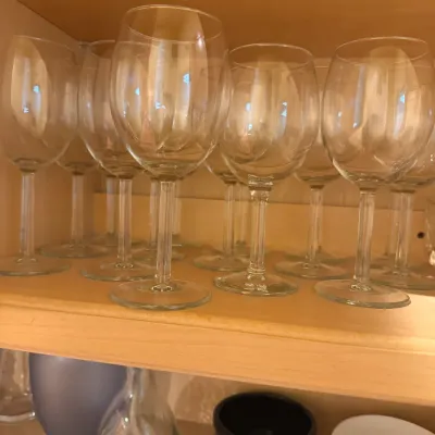 Collection of clear glass stemware arranged on a wooden cabinet shelf.