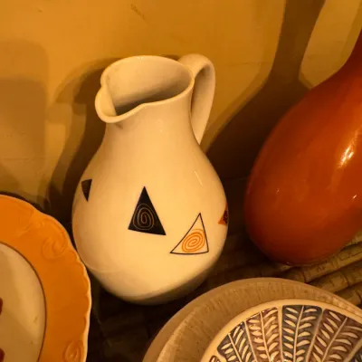 White ceramic pitcher featuring abstract geometric triangular motifs with spiral centers, displayed alongside various vintage ceramics.