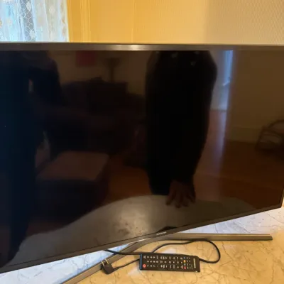 Samsung flat-screen television with original remote control and silver-tone stand, resting on a marble surface.