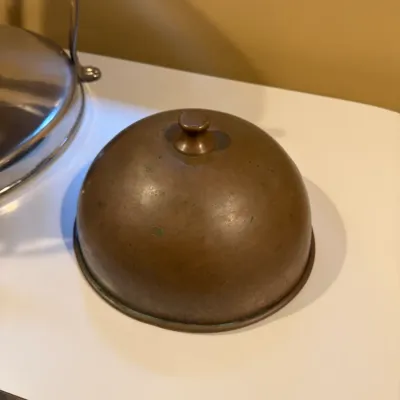 Vintage brass or bronze domed cloche food cover with a top finial handle, showing natural aged patina.