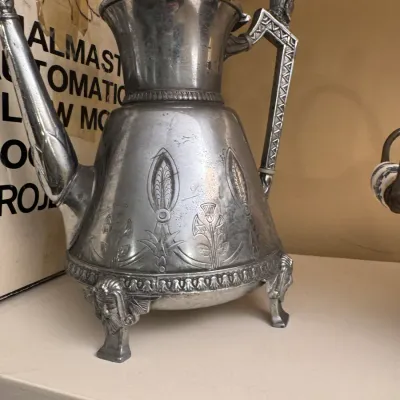 Antique Egyptian Revival silver-plated coffee server featuring engraved floral motifs, a winged figure finial, and detailed figural feet.