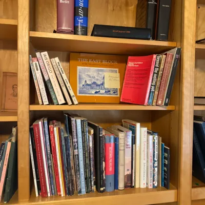 Wooden bookcase filled with various hardcover and paperback books, reference guides, and framed artwork.