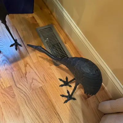 Pair of dark cast iron crane statues standing on a hardwood floor, featuring detailed feather textures and tall legs.