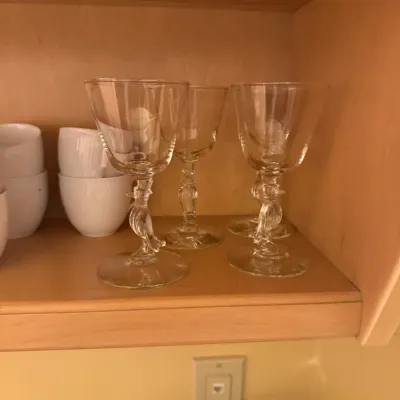 Set of clear glass wine or cocktail stems featuring figural bird-shaped pedestals, displayed on a wooden cabinet shelf.