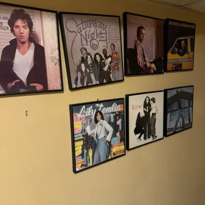 Collection of framed vintage vinyl album covers displayed on a wall, including Bruce Springsteen, Saturday Night Live, Lily Tomlin, and...