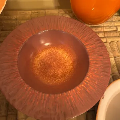 Mid-century studio pottery wide-rimmed bowl featuring a textured, radially carved dusty rose rim and an earthy orange-dappled center.