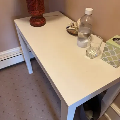 Simple off-white Parsons-style accent table, displaying a red carved lamp base and various small tabletop items.