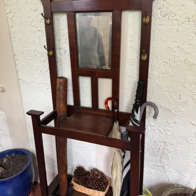 Antique Arts and Crafts style dark wood hall tree featuring a central mirror, brass coat hooks, integrated umbrella stands, and textured...