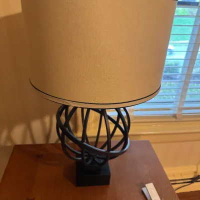 Modern table lamp with a dark metal armillary-style open sphere base and a large beige drum shade.
