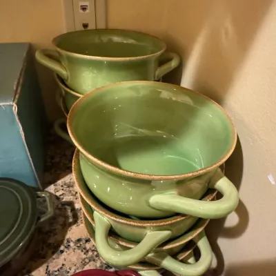 Stack of green glazed ceramic soup bowls with side handles and tan trim.