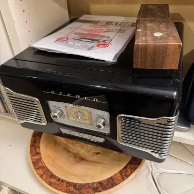 TEAC SL-A100 retro-style black music system with built-in turntable and radio, sitting on a lazy susan alongside its manual and record...