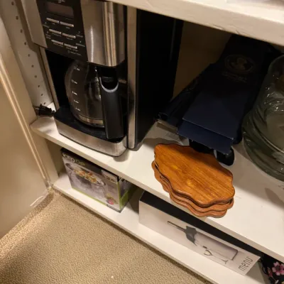 Mr. Coffee 12-cup programmable coffee maker in stainless steel and black finish, displayed on a closet shelf alongside wooden coasters...