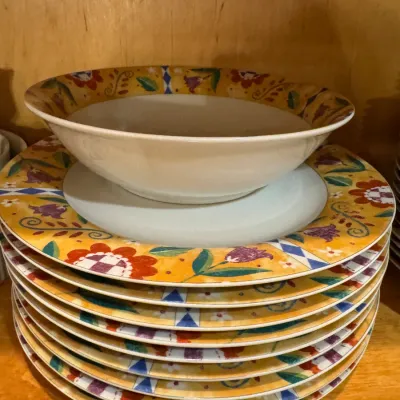 Stack of ceramic dinner plates and a matching serving bowl featuring a colorful floral rim pattern on a yellow background.