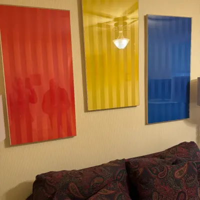 Set of three vintage framed primary color stripe acrylic wall art panels in red, yellow, and blue, mounted above a paisley sofa.