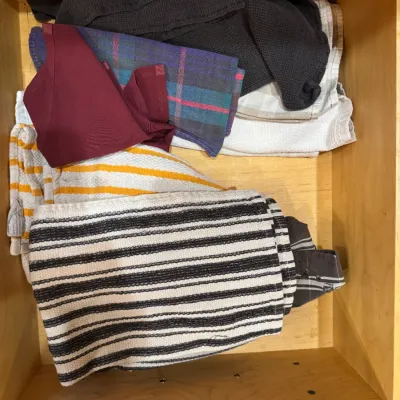 Assorted folded kitchen linens and dishtowels in a wooden drawer.