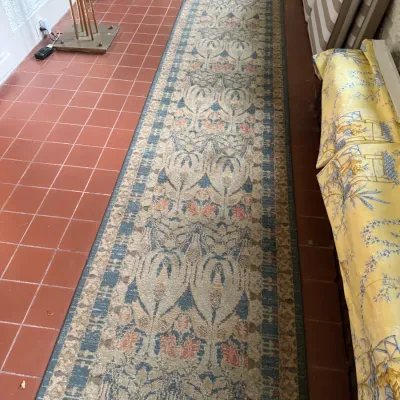 Long woven runner rug with an ornate floral and damask pattern in blue, beige, and terracotta tones, laid across a red tile floor.