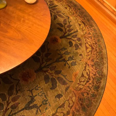 Large circular area rug featuring a botanical tree motif and floral border in earthy olive, gold, and brown tones.