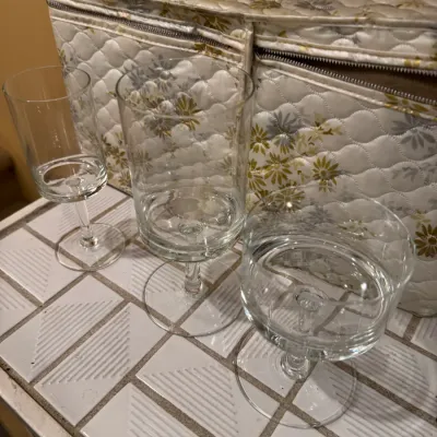 Set of three vintage clear glass stemware pieces displayed in front of a quilted floral storage chest.