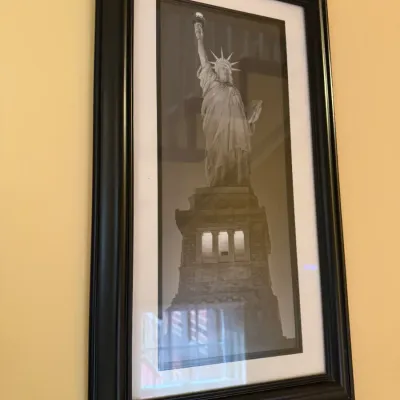 Framed black-and-white photograph of the Statue of Liberty, set in a white mat and dark wood frame.