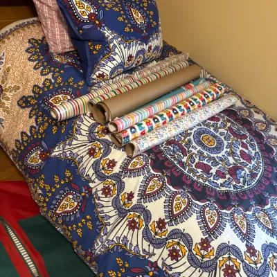 Collection of assorted gift wrapping paper rolls displayed on a bed dressed with a bohemian paisley-patterned duvet and pillow shams.