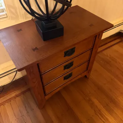 Mission or Craftsman-style oak three-drawer nightstand with butterfly joint details and black metal hardware, topped with a contemporary...