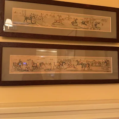 Pair of framed vintage panoramic equestrian art prints depicting horse racing and steeple chasing in dark wooden frames.