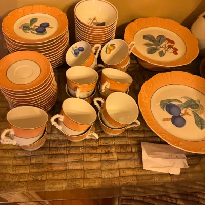 Vintage ceramic dinnerware set featuring peach-orange wide rims and botanical fruit motifs, including plates, teacups, and bowls.