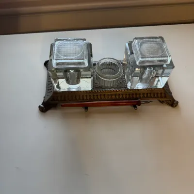 Vintage brass inkstand featuring double heavy glass inkwells with matching lids, a central glass dish, and an included dip pen.