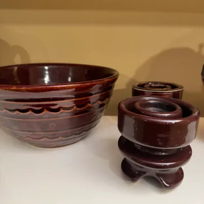 Vintage dark brown glazed stoneware mixing bowl with scalloped band detail, displayed alongside a matching porcelain insulator and crock.