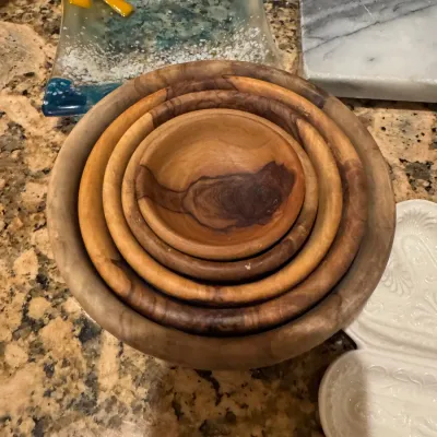 Set of four nesting handcrafted olive wood bowls displaying natural grain variations, displayed alongside decorative glass and ceramic...