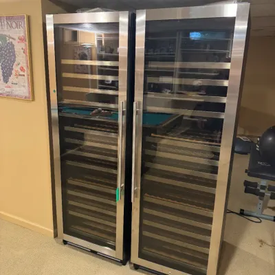 Pair of tall stainless steel wine refrigerators with glass doors and pull-out wooden racks.