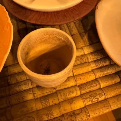 A small ceramic pot or vessel displayed alongside stoneware plates on a wine cork-topped table.