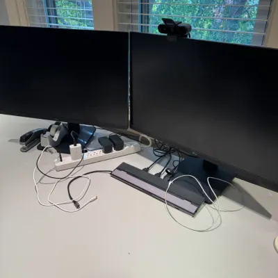 Dual LG computer monitors setup on a desk with a webcam, docking station, power strip, and office accessories.