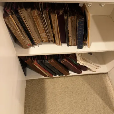 Collection of vintage 78 RPM record albums with worn covers, organized on white cabinet shelves.