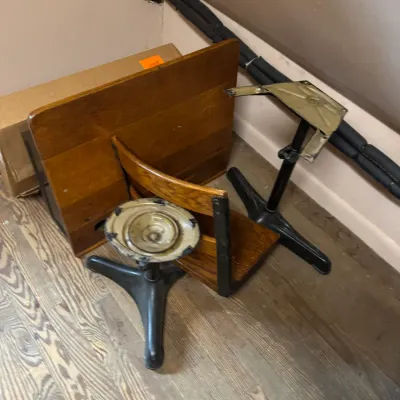 Disassembled vintage school desk featuring a wooden writing top, curved chair back, and heavy cast iron bases.