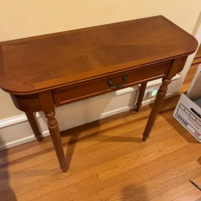Traditional wooden console table featuring a single front drawer with a brass pull, rounded edges, and fluted legs.