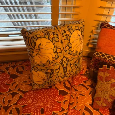 William Morris Arts and Crafts style floral accent pillow, sitting on a window seat cushion with a matching warm-toned botanical print.