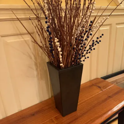 Tall dark ceramic floor vase filled with decorative branches and faux berry stems, displayed on a wooden bench.