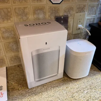 White Sonos One smart speaker displayed next to its original retail packaging box.