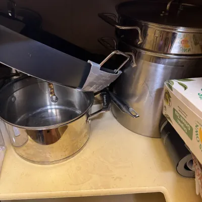 Assorted stainless steel and non-stick cookware stored inside a cabinet, including a Cuisinart pot and large stockpots.