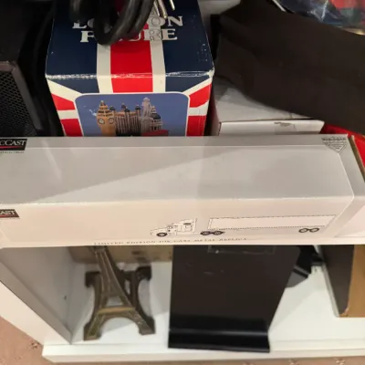 Die-cast metal replica tractor-trailer in original packaging, alongside souvenir figurines and power cords on a shelf.