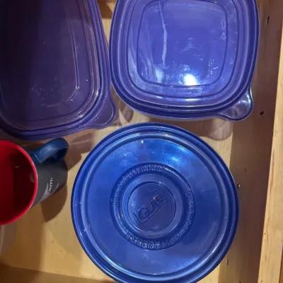 Selection of blue and purple plastic GladWare storage containers with matching lids in a wooden drawer.