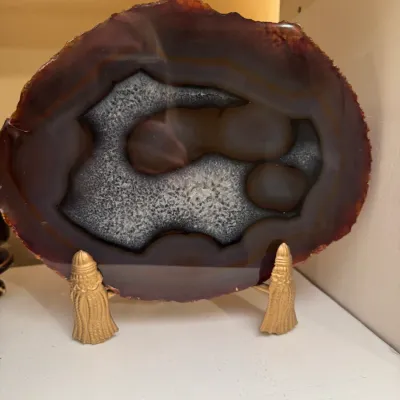 Polished agate geode slice displaying natural brown and grey banding, displayed on a decorative gold-toned metal easel stand.