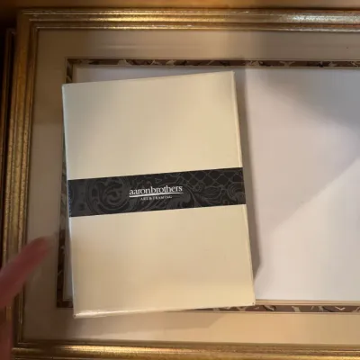 Gold-toned picture frame with double matting, accompanied by a packaged Aaron Brothers Art & Framing item.